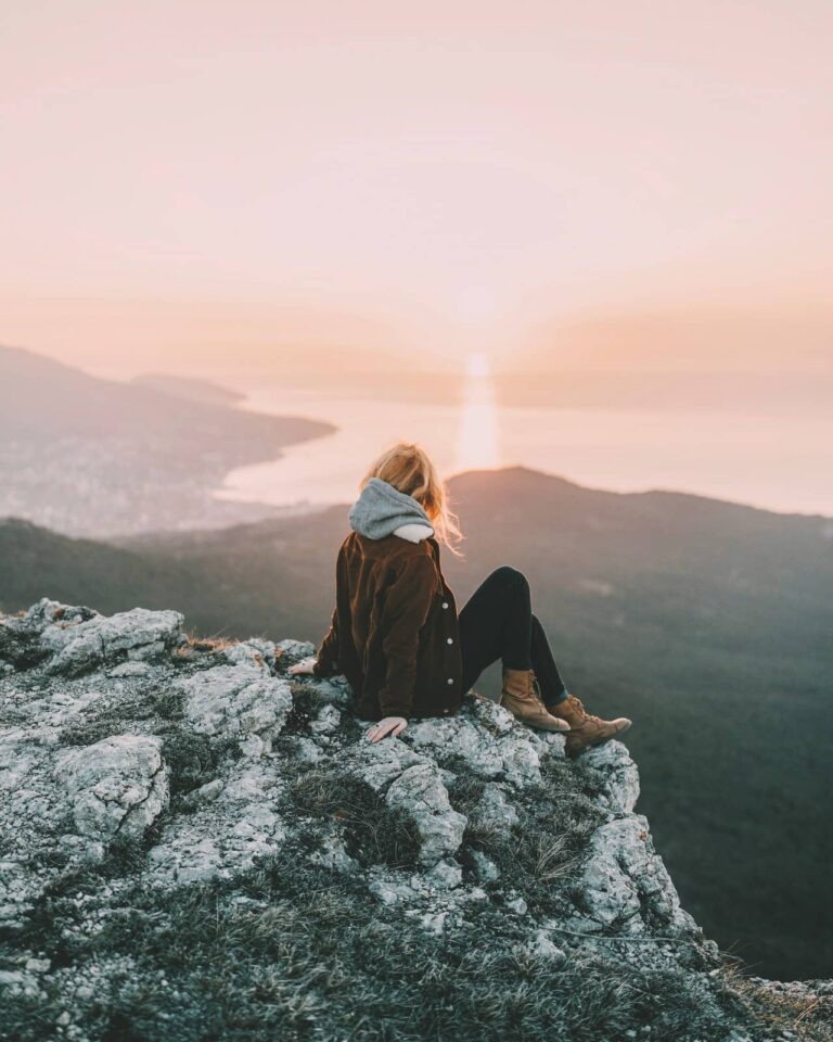 Femme assise sur un rocher contemplant les montagnes au lever du soleil